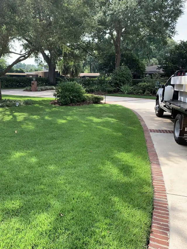 Manicured lawn with a curved brick-edged driveway and the rear of a company truck