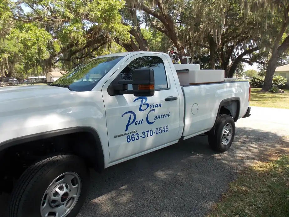 White Brian Pest Control pickup lettered with the office number, parked under live oaks