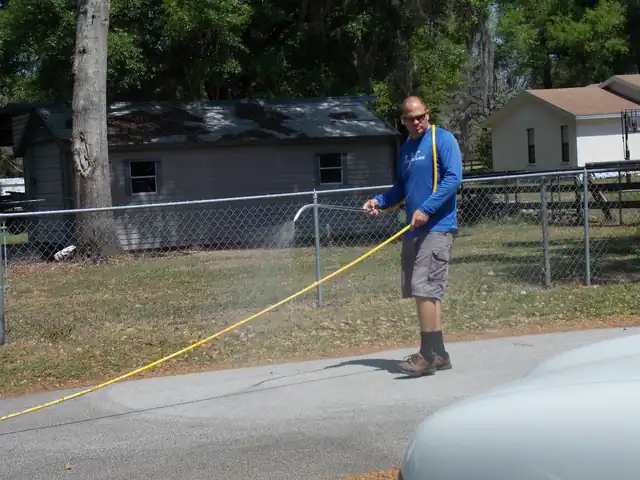 Technician spraying a fence line with a yellow hose