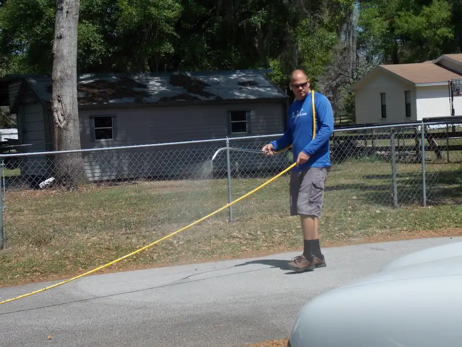 Technician spraying a fence line with a yellow hose