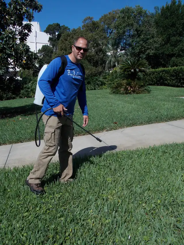 Technician with a backpack sprayer treating a green front lawn